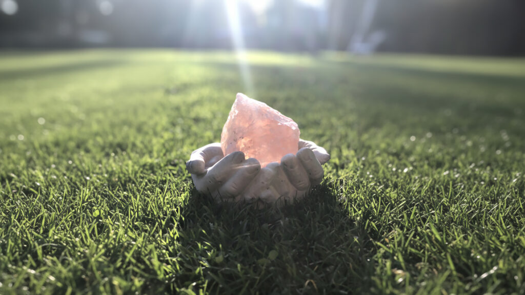 Rosenquarz liegt in einer kleinen Steinschale auf Gras im Gegenlicht der Sonne