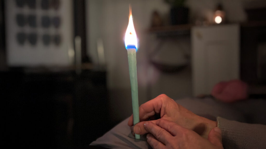 Hand hält eine brennende grüne Kerze im Halbdunkel